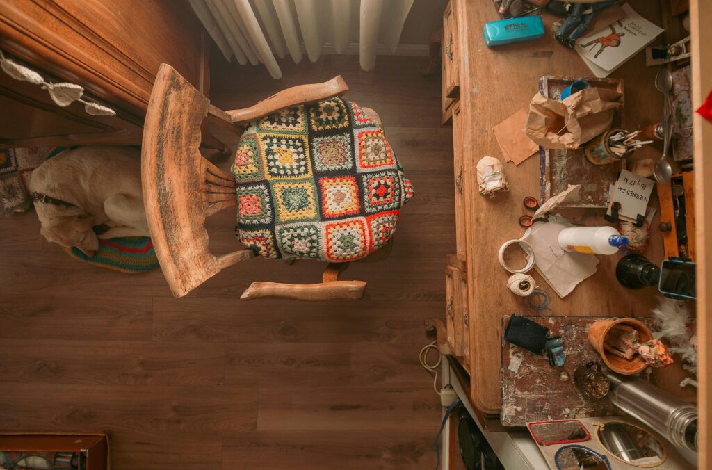 Top-down view of a craft room with a colorful quilted chair, cluttered desk, and a sleeping dog.